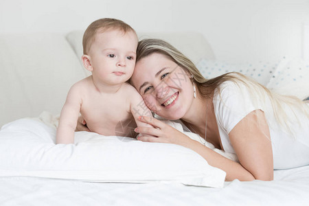 快乐微笑的小男孩和母亲躺在枕头上看着图片