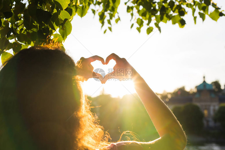 女在日落时展示心脏的形状图片