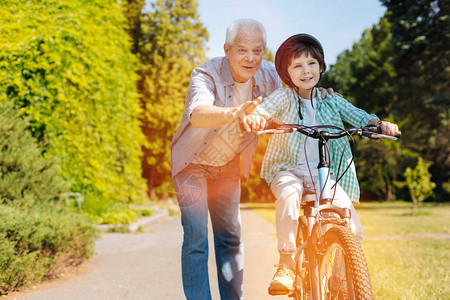 友善热情的年青绅士教他孙子如何骑自行车图片