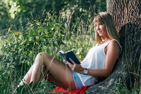 坐在公园一棵树下看书的年轻女图片