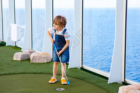 小男孩在游轮上打迷你高尔夫度假时玩得开图片