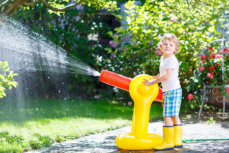 有趣的小男孩在炎热和阳光明媚的夏日玩花园软管洒水器图片