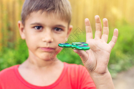 躁动不安一个男孩玩扭在他的手在户外的微调儿童抗应激玩具的趋势背景