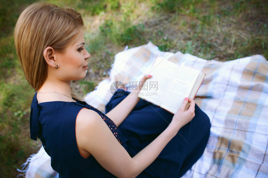 穿着深蓝色裙子的金发女孩坐在格子上阅读这本书假期节日图片