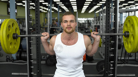 在健身房进行力量训练t恤做杠铃深蹲的家伙健美运动图片