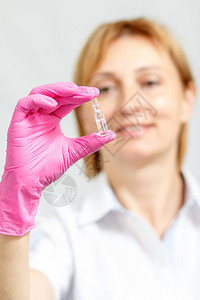 使用粉色手套微笑的女医生手持带有药剂背景图片