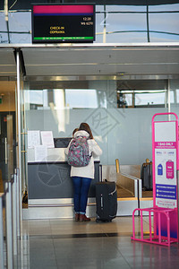 年轻女子在机场登记旅行者有一个小行李一个背包图片