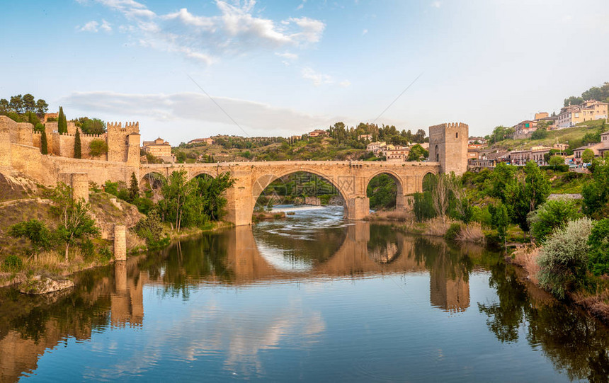 西班牙托莱多的美丽风景横跨平静河的石桥湛蓝的天空倒映在水晶般清澈的水中背景中的大堡垒和乡间别墅欧洲的图片