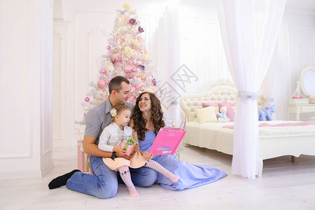 年轻快乐的父母和小女儿阅读和考虑孩子的粉红色书图片