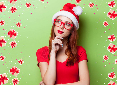 身着圣诞老人帽子和绿背景红眼镜的年轻红头图片
