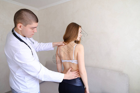 专业的男医生建议并检查来接待的可爱女孩的背部并感到背部不适穿着欧式图片