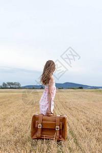 在秋季小麦田穿着经典服装和旅行李箱的小姑娘图片