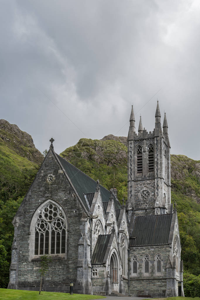 Abbey土地上的小型灰色新哥特教堂与岩石绿山和银色天空相对立图片