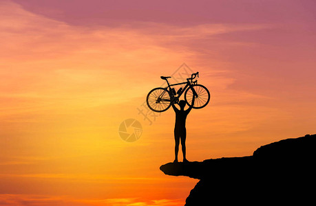 以日落的黄昏背景在悬崖山顶上举起脚踏车来图片