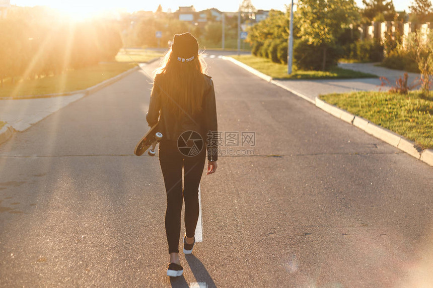 美丽的年轻时尚感女郎在夏天晚上与长板一起在路上散步玩得开心点展示她穿黑图片