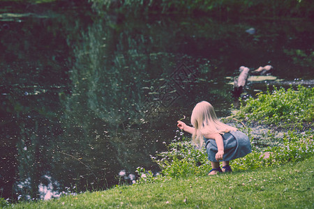 对穿着衣服坐在河边采花的小高加索女孩的近视夏图片