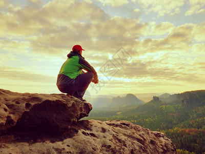 穿着绿色黑夹克的徒步旅行者坐在岩石山峰上图片