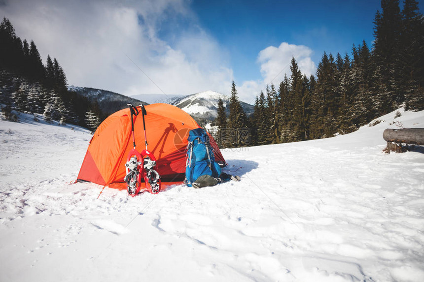 在橙色帐篷附近的雪上有一个雪鞋和背包站图片