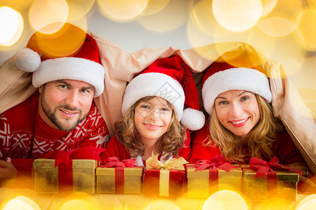 幸福的家庭的肖像躺在毯子下的毛毯下戴着圣诞老人图片