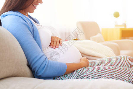 在沙发上放松时抱着手放在肚子上的孕妇快图片