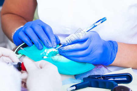 一位身穿白色医疗制服的年轻女牙医和她的助手在牙科工具的背景下图片