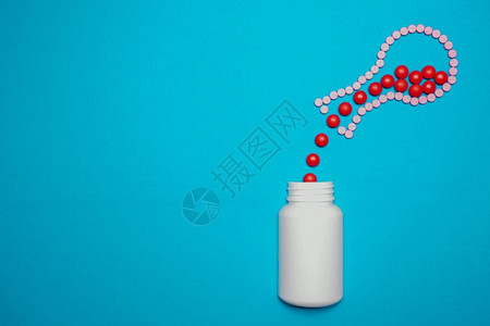 红色药丸从圆底酒瓶中溢出以蓝色背景将药丸放入白瓶背景图片
