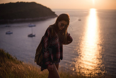 在日落时看着大海或洋的时髦尚女旅行者图片