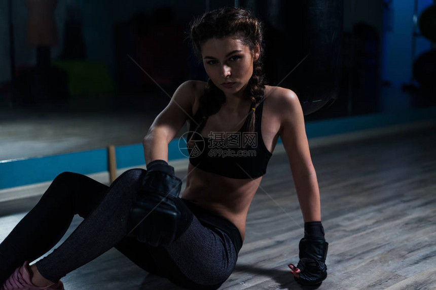 年轻拳击手女孩在训练前戴着拳击手套坐在黑暗体图片