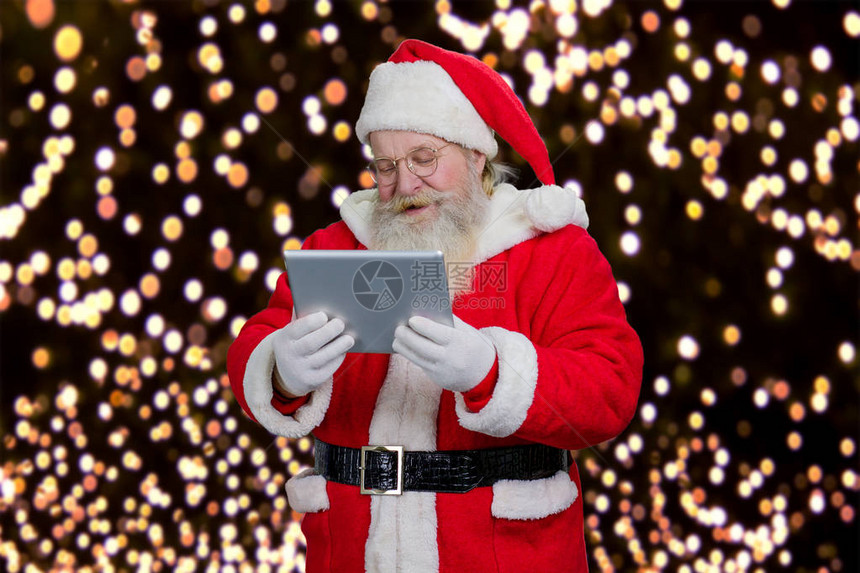 圣诞老人在平板电脑上阅读高级圣诞老人拿着数字平板电脑和阅读图片