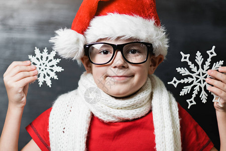 戴着圣诞老人帽子和眼镜的小男孩手里拿着塑料雪花图片
