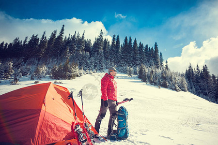 登山者在登山前在帐篷附近收集设备营地附近背着包的男人冬天穿雪鞋和图片