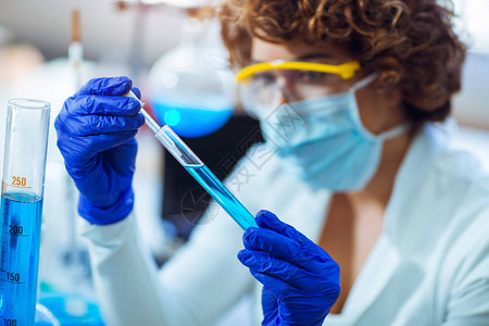戴防护眼镜和手套的年轻女科学家在科学化实验室用玻璃吸管将液体图片