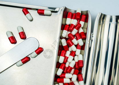 红色白抗生素胶囊药丸在不锈钢制毒托盘上的顶端景象图片