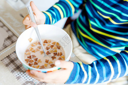 早餐或午餐吃自制麦片的孩子手的特写儿童健康饮食在托儿所学校食堂或家里碗特写镜头用牛奶和麦片拿背景图片