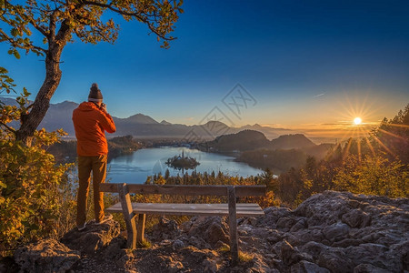 身穿橙色夹克和帽子的摄影师旅行者拍摄朱利安阿尔卑斯山的秋季日出全景图片
