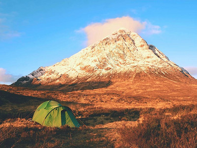 1021米高的StobDearg山雪锥下河边草地上的绿色旅游帐篷苏格兰高地是一个阳光明媚的冬日干草和石南花灌木徒背景