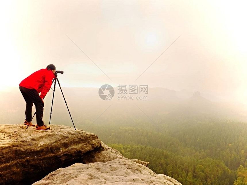 调查dslr数码相机取景器的摄影师站在三脚架上艺术家拍摄山区和多云的景观男人在拍摄自然照片时检查屏幕上的照片他的图片