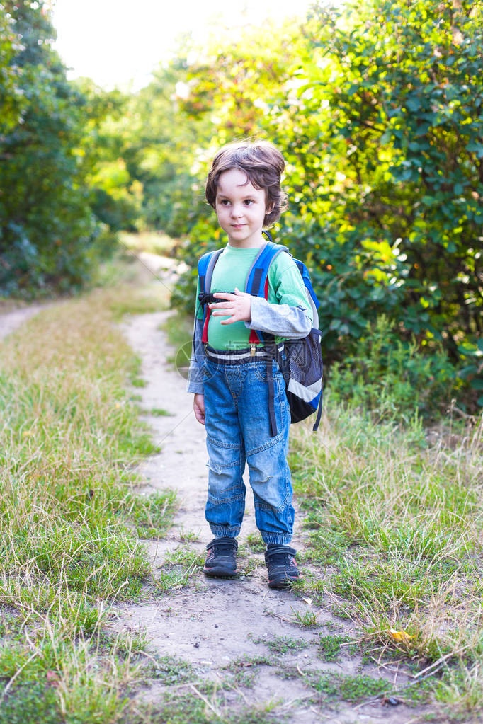一个背着书包的男孩正穿过森林孩子在旅行孩子站在公园里的一条小路上图片