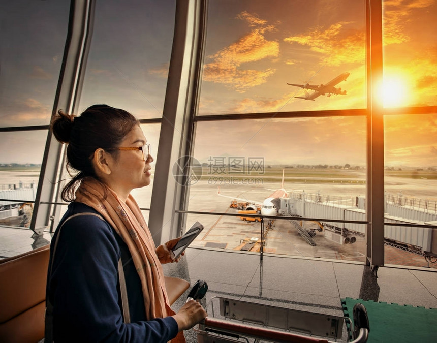 手持智能手机的女站在机场航站楼和客机图片