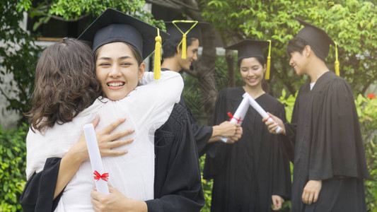 女孩学生与毕业礼服和帽子拥抱父母图片