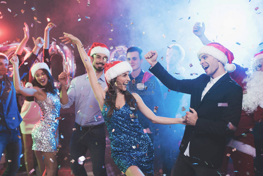 年轻夫妇在晚会上玩得很开心他们戴着圣诞老人帽跳舞在跳舞的背景下他们的朋友他们图片