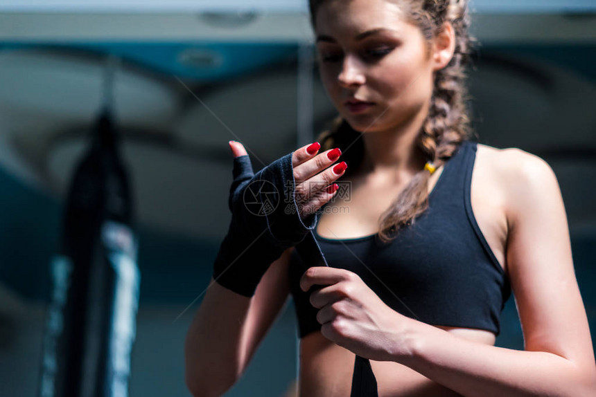年轻拳击手女孩在训练前用重拳背包贴上绷带图片