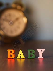 婴儿由木字母颜色制成的英文字母木桌和老式闹钟和背景上的字母婴图片