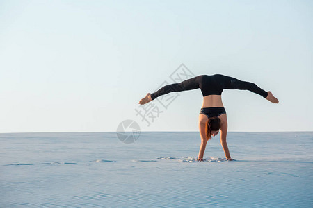 年青女在练习反向平衡瑜伽在沙滩上站立图片