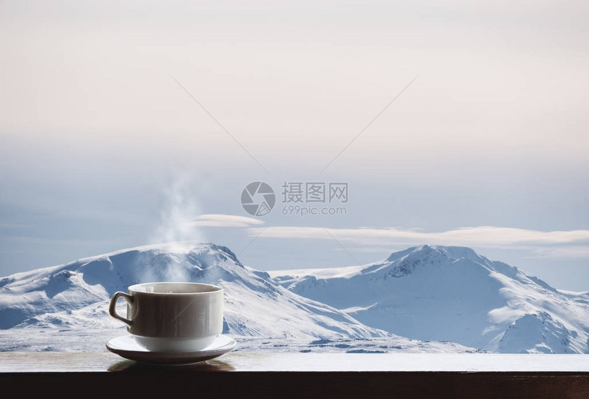 一杯热的饮料与蒸汽在木桌和雪盖帽的山看法早晨图片