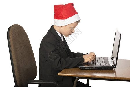穿着圣诞老人西装的家伙拿着笔记本电脑坐在桌子上图片