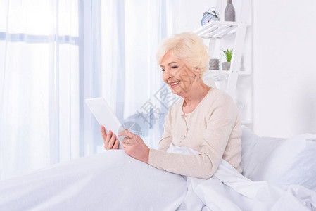家中躺着平板电脑的幸福老年妇女的侧视图图片