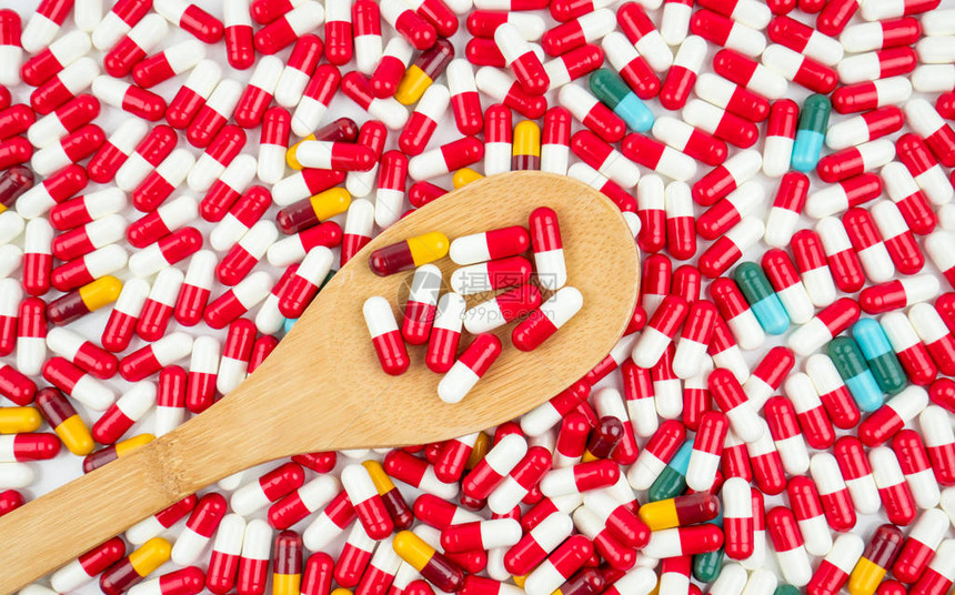 五颜六色的抗生素胶囊丸和白色背景上的木勺耐药概念具有合理和全球保健理念的抗图片