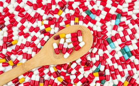 五颜六色的抗生素胶囊丸和白色背景上的木勺耐药概念具有合理和全球保健理念的抗背景图片