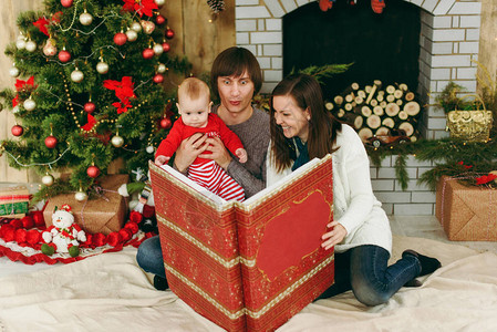 年轻俏皮快乐的父母带着一个可爱的小男孩在家里装饰的房间里读大红书圣诞好心情新年生活方式家庭背景图片